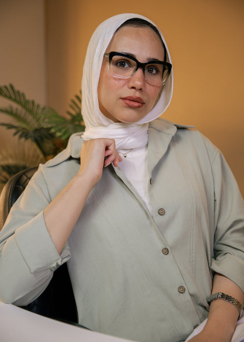 Woman wearing a light green shirt and white hijab with a blurred background
